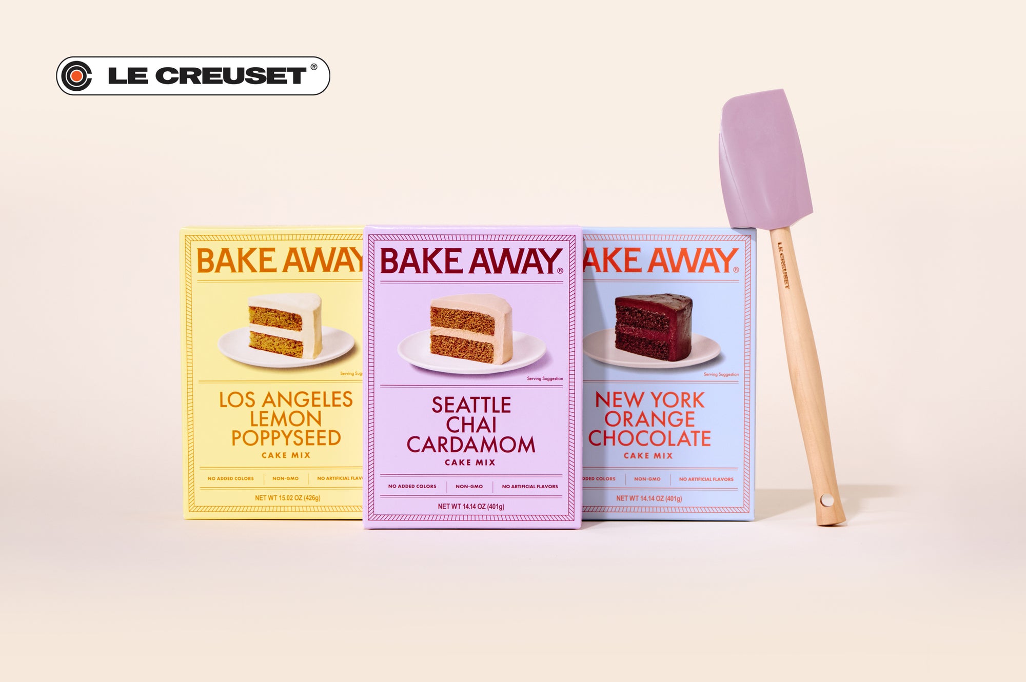 Three boxes of 'Bake Away' cake mixes with a spatula on a light background, featuring Le Creuset branding.