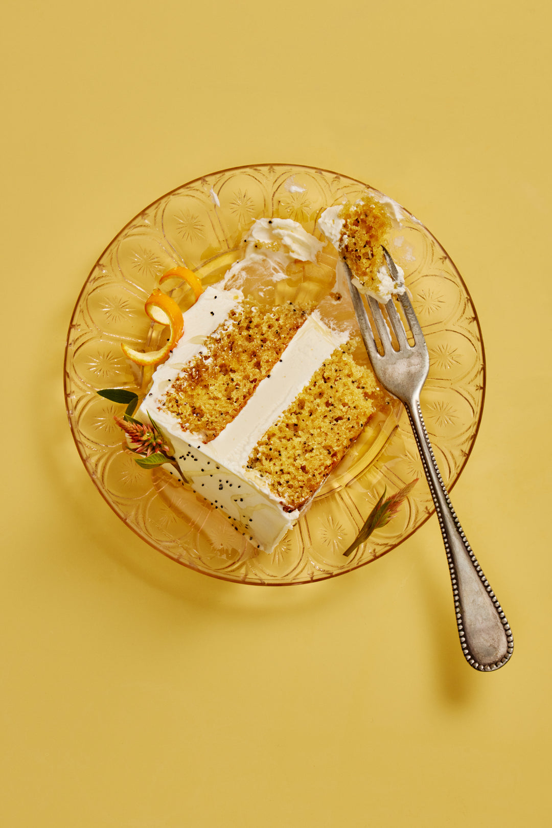 Slice of lemon poppyssed cake on a decorative glass plate with a fork on a yellow background