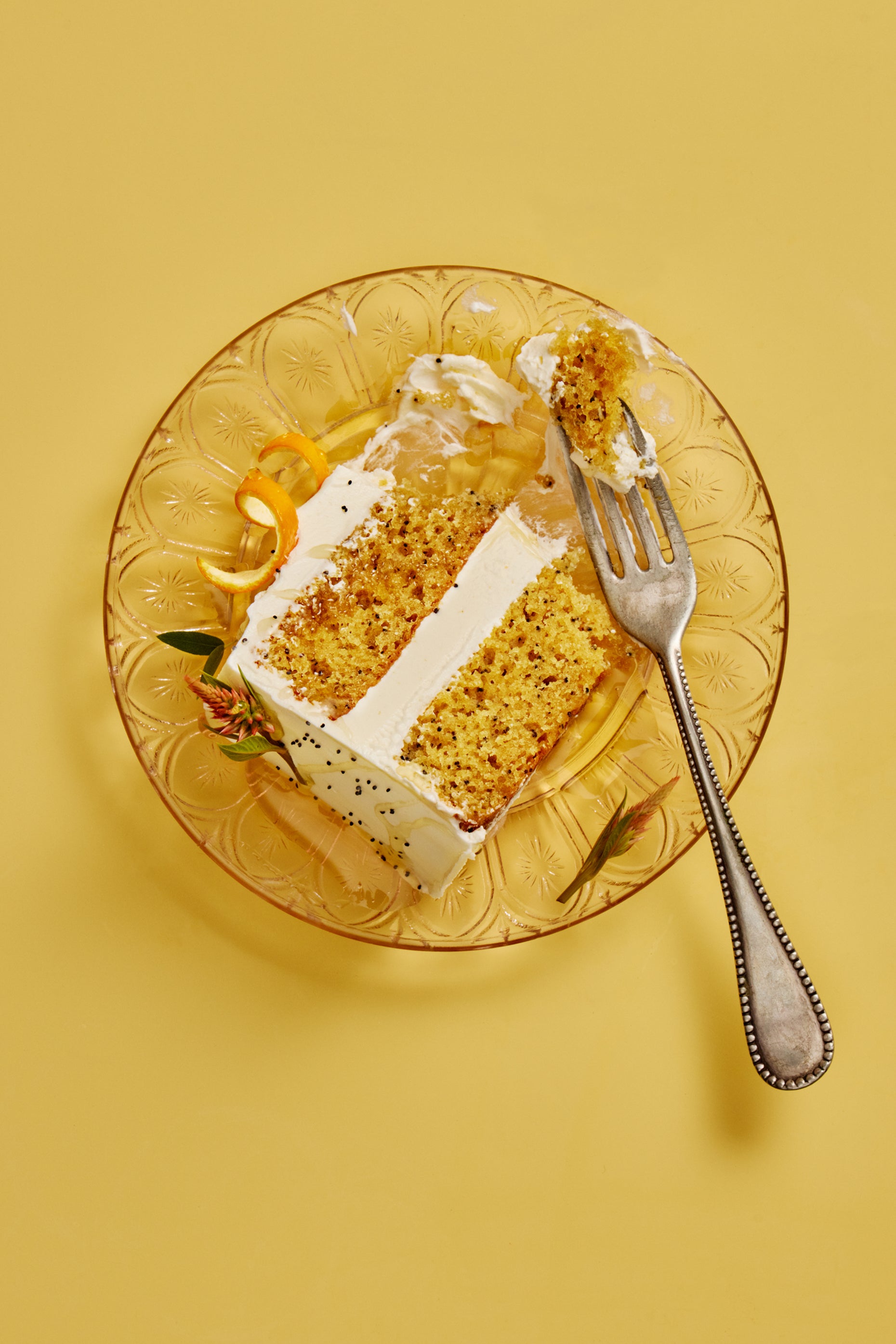 Slice of lemon poppyssed cake on a decorative glass plate with a fork on a yellow background