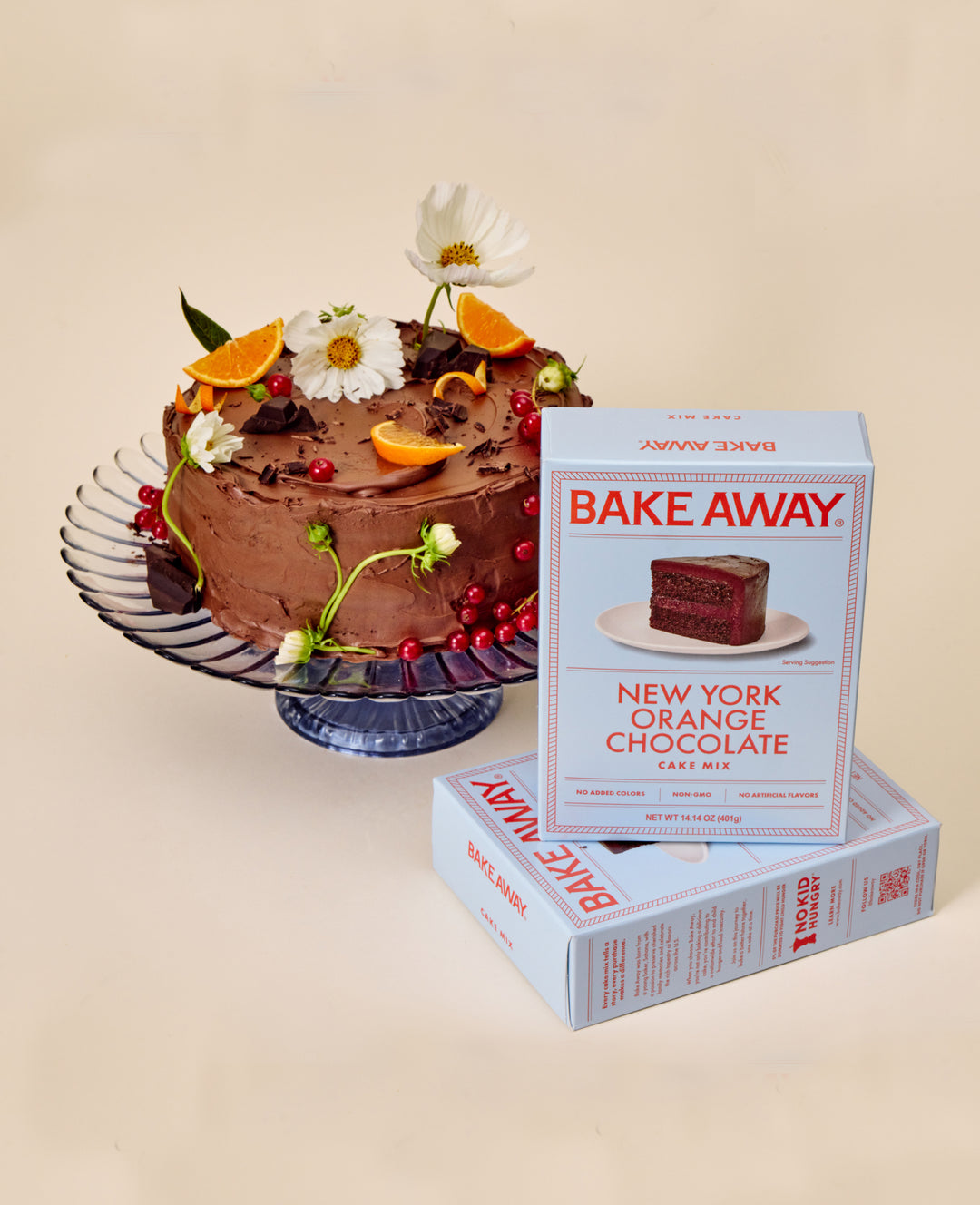 New York Orange Chocolate Cake mix boxes are stacked next to a highly decorated chocolate and orange cake. 