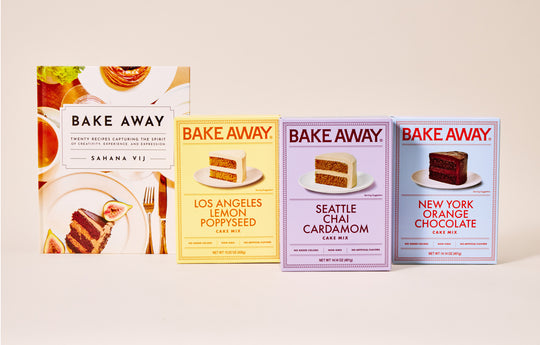Three 'Bake Away' cake mix boxes with different flavors on a beige background next to a Bake Away cookbook by Sahana Vij