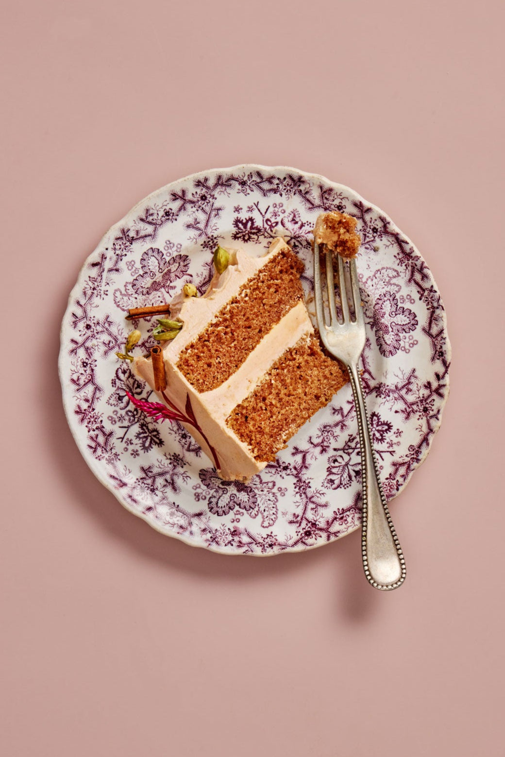 Slice of layered Seattle Chai Cardamom cake on a decorative plate with a fork against a pink background