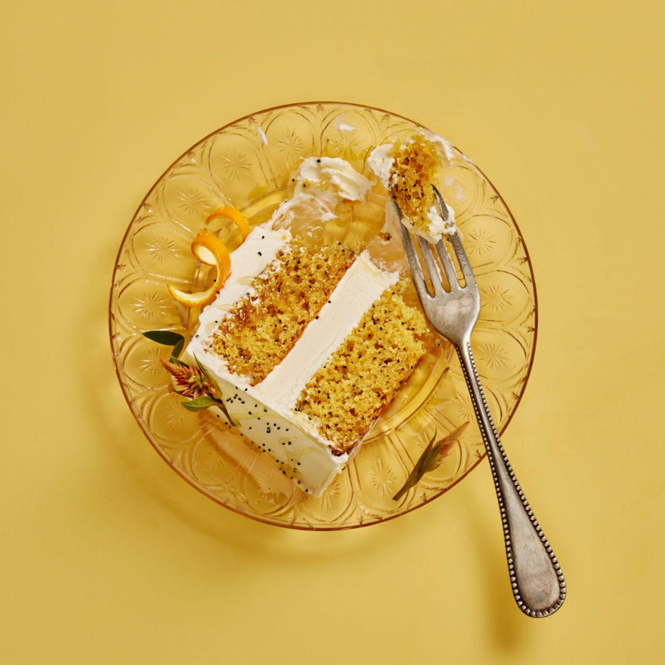 Slice of cake on a decorative glass plate with a fork on a yellow background