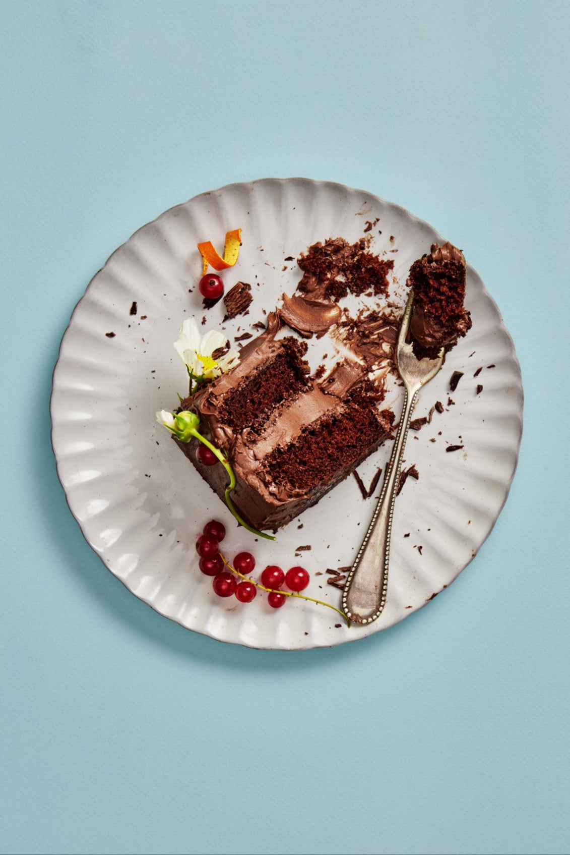 Slice of New York Orange chocolate cake on a white plate with berries against a light blue background