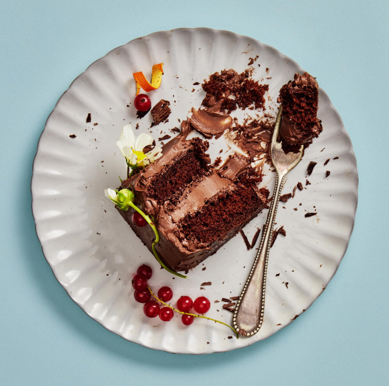 Slice of chocolate cake on a decorative plate with berries and a fork, against a light blue background