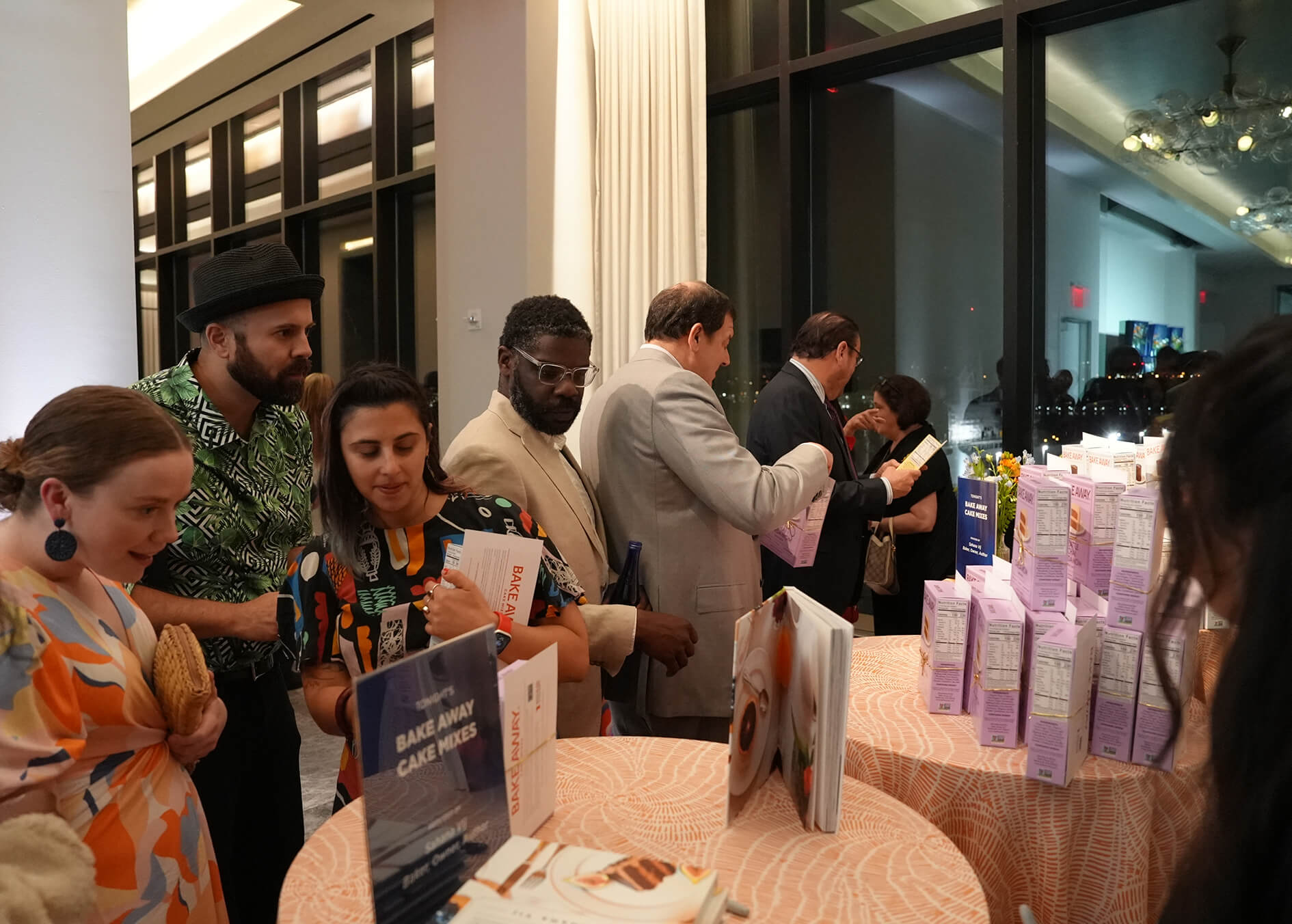 People interacting around a table with promotional materials and products in an indoor setting.
